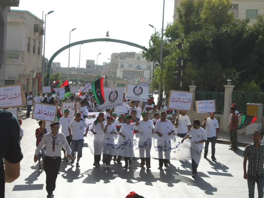 شباب يسيرون حاملين لافتات وأعلامًا إحياءً لذكرى ثورة 17 فبراير